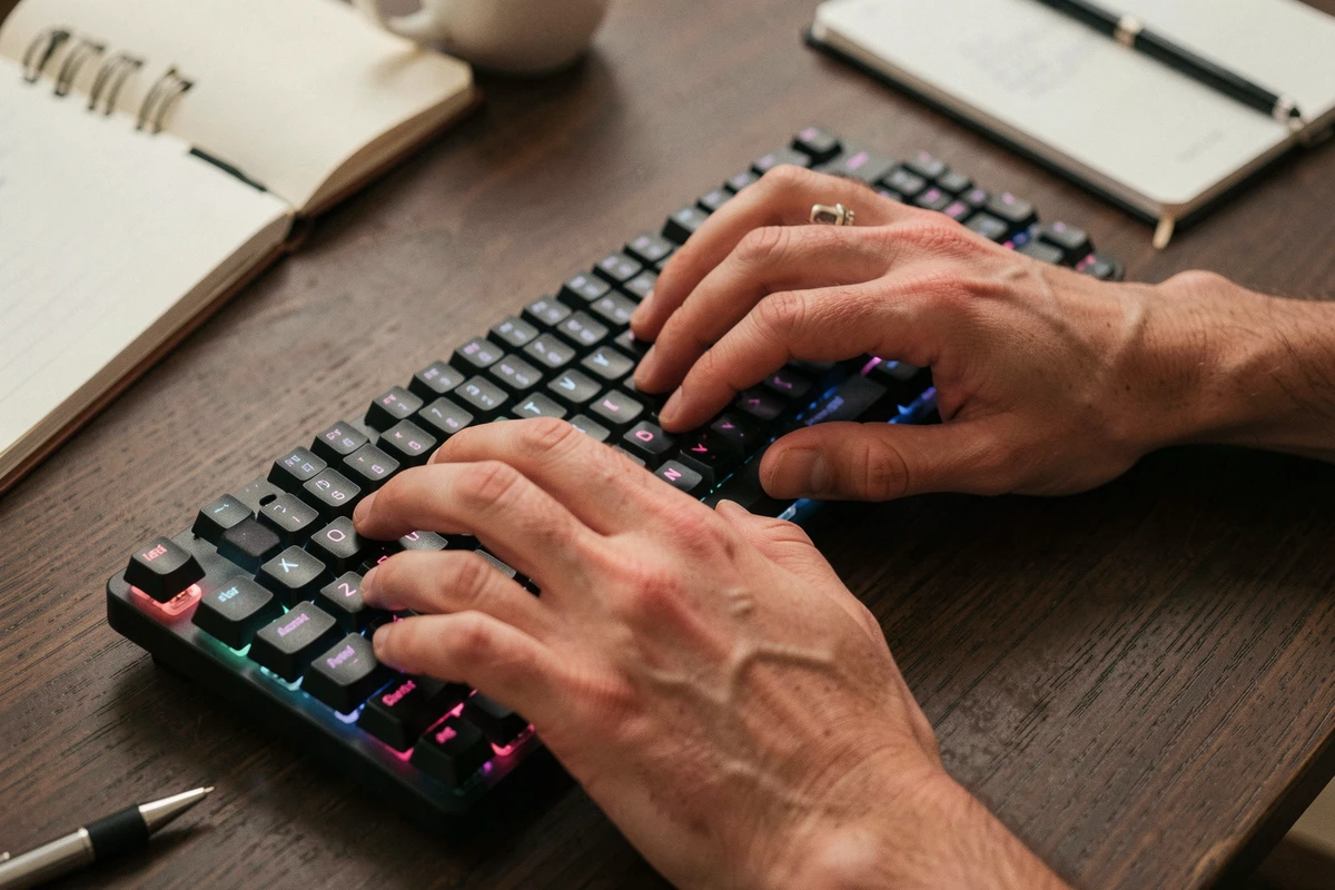 Gros plan des mains en train de taper rapidement sur un clavier mécanique rétroéclairé vu de dessus